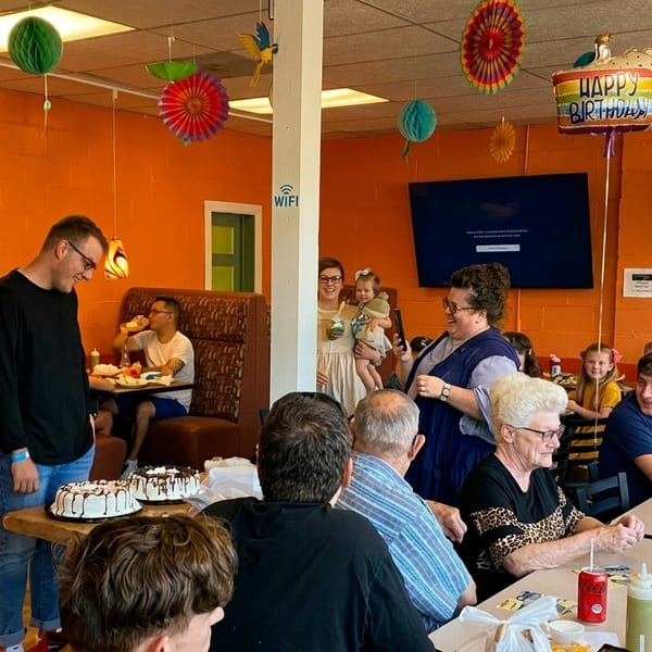A lively birthday party with many people gathered around tables in a restaurant with orange walls.