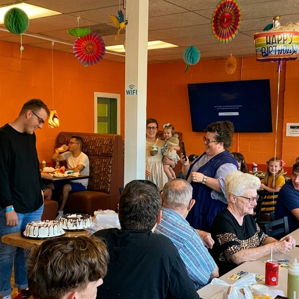 A lively birthday party with many people gathered around tables in a restaurant with orange walls.