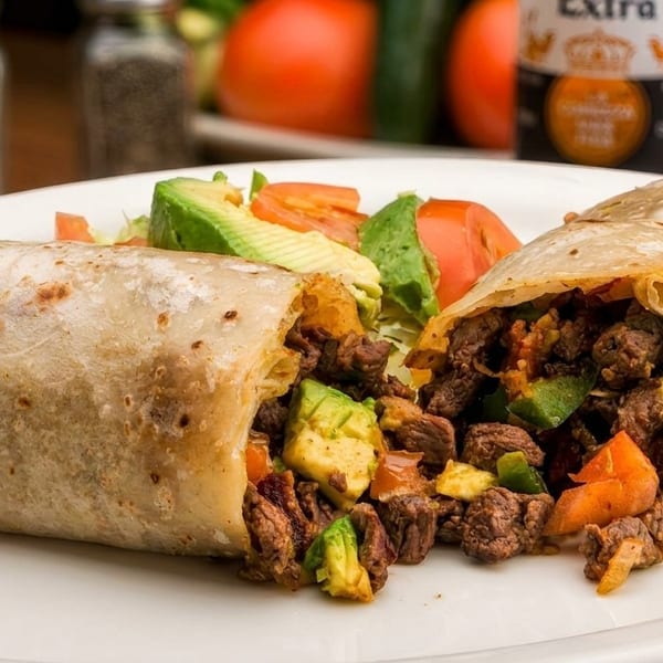 Two large burritos, one cut open to show steak, avocado, and peppers, with a side salad.