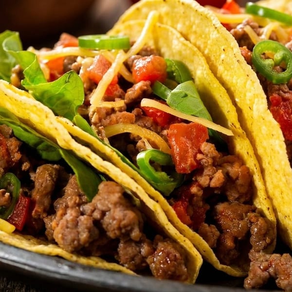 Three hard-shell tacos filled with seasoned ground beef, shredded cheese, lettuce, tomatoes, and jalapeños.